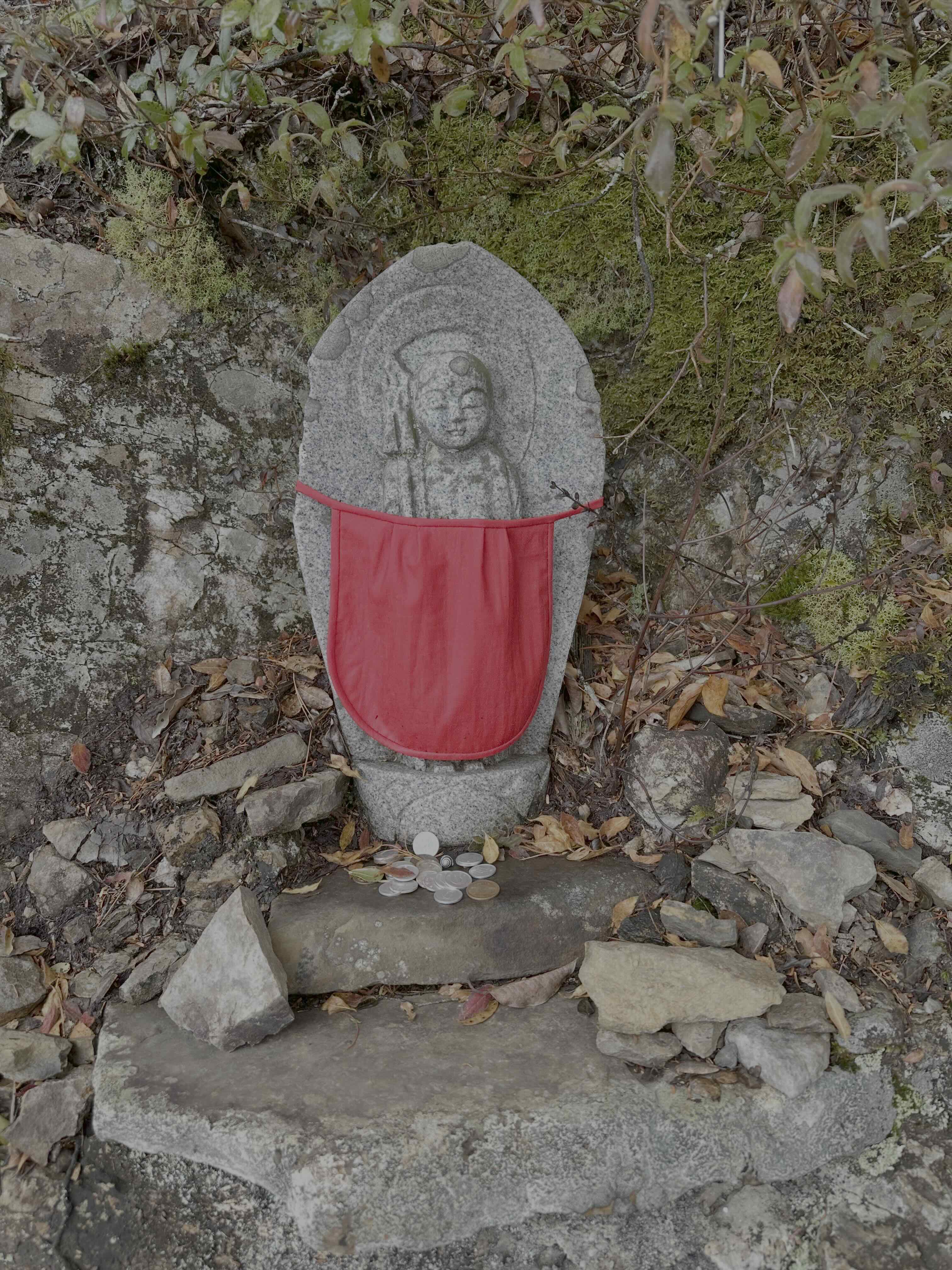 A Jizo statue with a red bib tied across the front.
